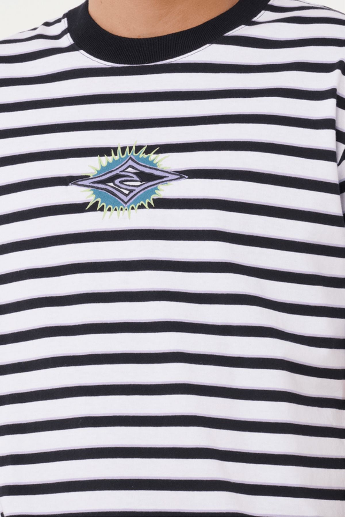 A person wears a Rip Curl Raw Energy Stripey Tee with black and white stripes, a colorful geometric patch, and an embroidered chest logo featuring an "S" emblem. Only the upper torso is shown.