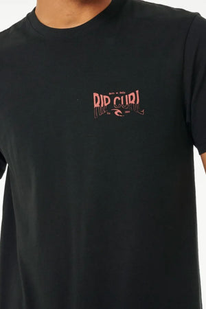 A person wears the Rip Curl Affinity Tee, a classic black 100% cotton t-shirt with a small pink βRip Curlβ logo and wave on the left chest. Only their upper torso is visible.