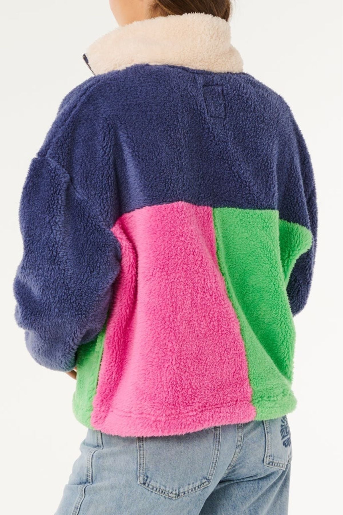 A person wearing the Rip Curl Block Party Polar Fleece, featuring blue, pink, and green panels, paired with light blue jeans. The photo from behind highlights the jacket's cozy polyester microfleece fabric.