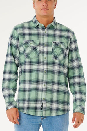 A person wears the Rip Curl Count Flannel Shirt in light green and black plaid with two chest pockets, paired with light blue jeans, standing against a plain white background.