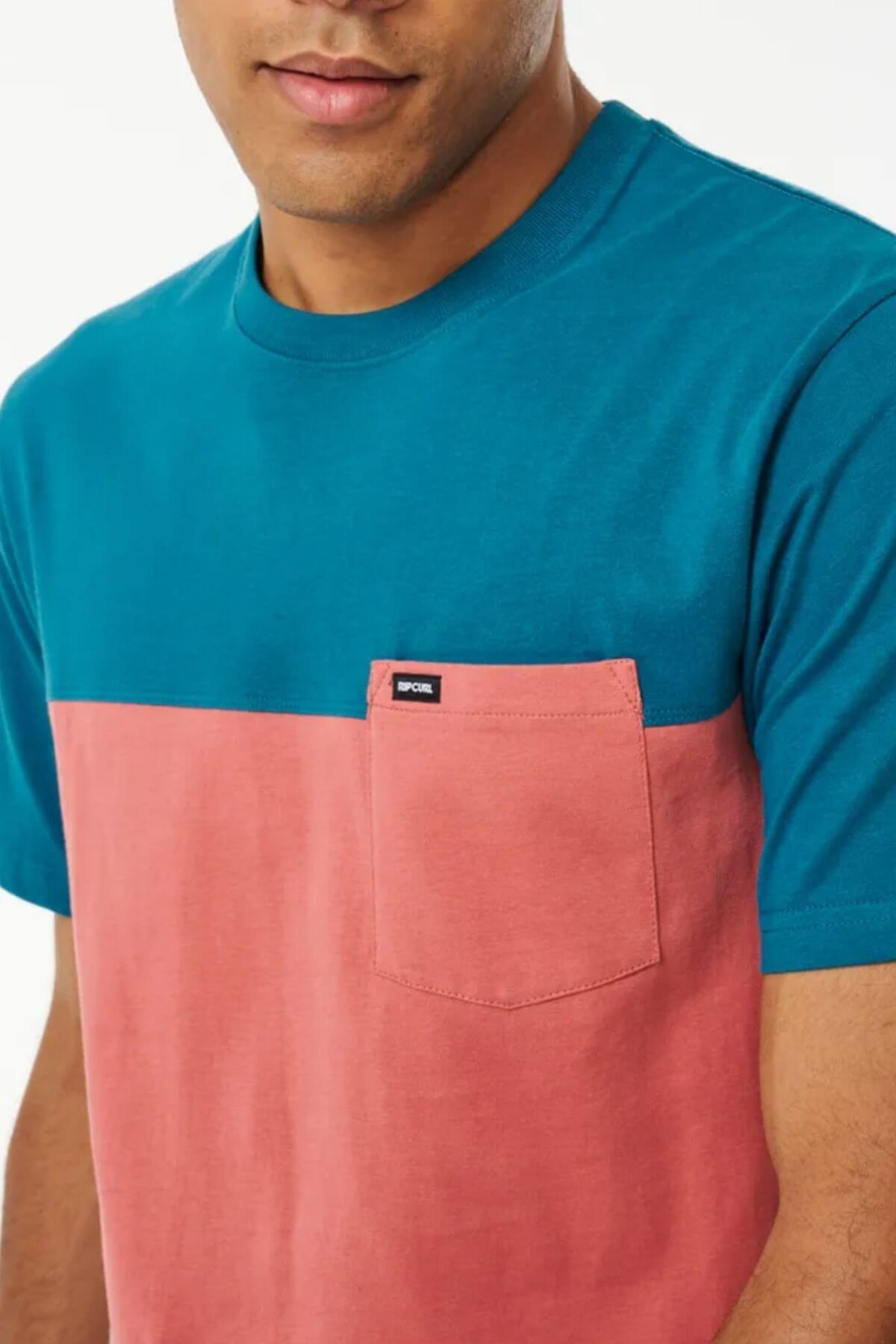 Wearing the Rip Curl Divided Tee, a 100% cotton color-blocked shirt with teal sleeves and neckline, and a pink lower half featuring a chest pocket with a black tag. Only the person's lower face and upper torso are shown.