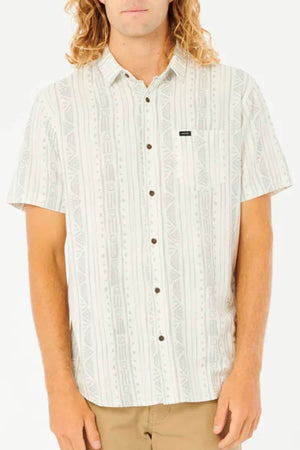 A person with long wavy blond hair wears a Rip Curl Nocturnal Short Sleeve Shirt, featuring a viscose linen blend and subtle geometric pattern, with khaki pants, standing against a plain white background.