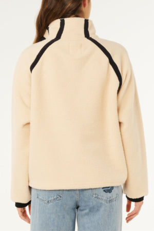 A person is seen from the back wearing the Rip Curl Surf Club Heritage Polar fleece jacket in light beige with black trim, paired with light blue jeans, set against a plain white background.