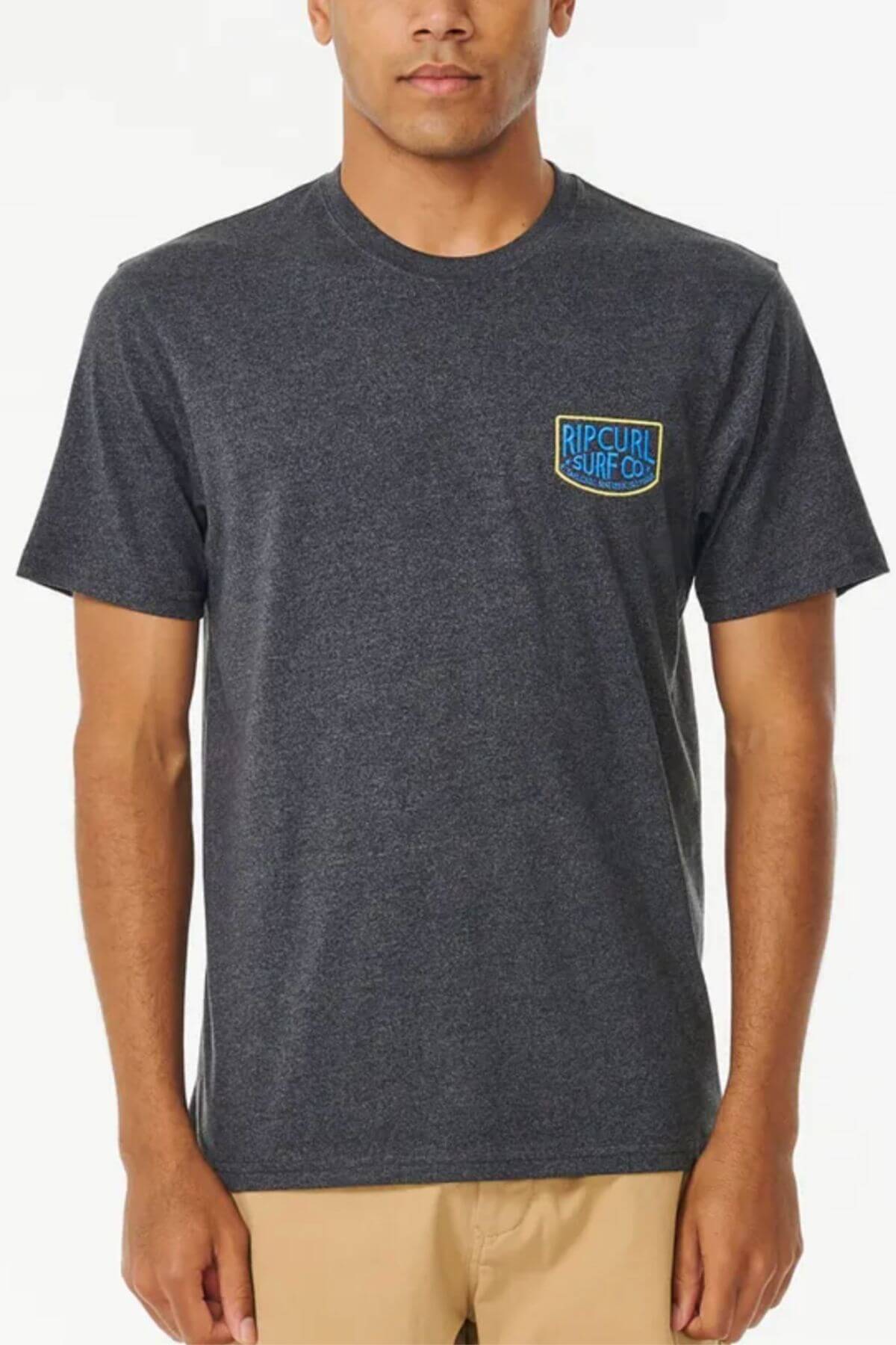 A person is styled against a plain background in light-colored pants, wearing the Rip Curl Too Easy Embroid Tee, made from 100% cotton in dark gray with an embroidered "Rip Curl Surf Co." logo on the left chest.