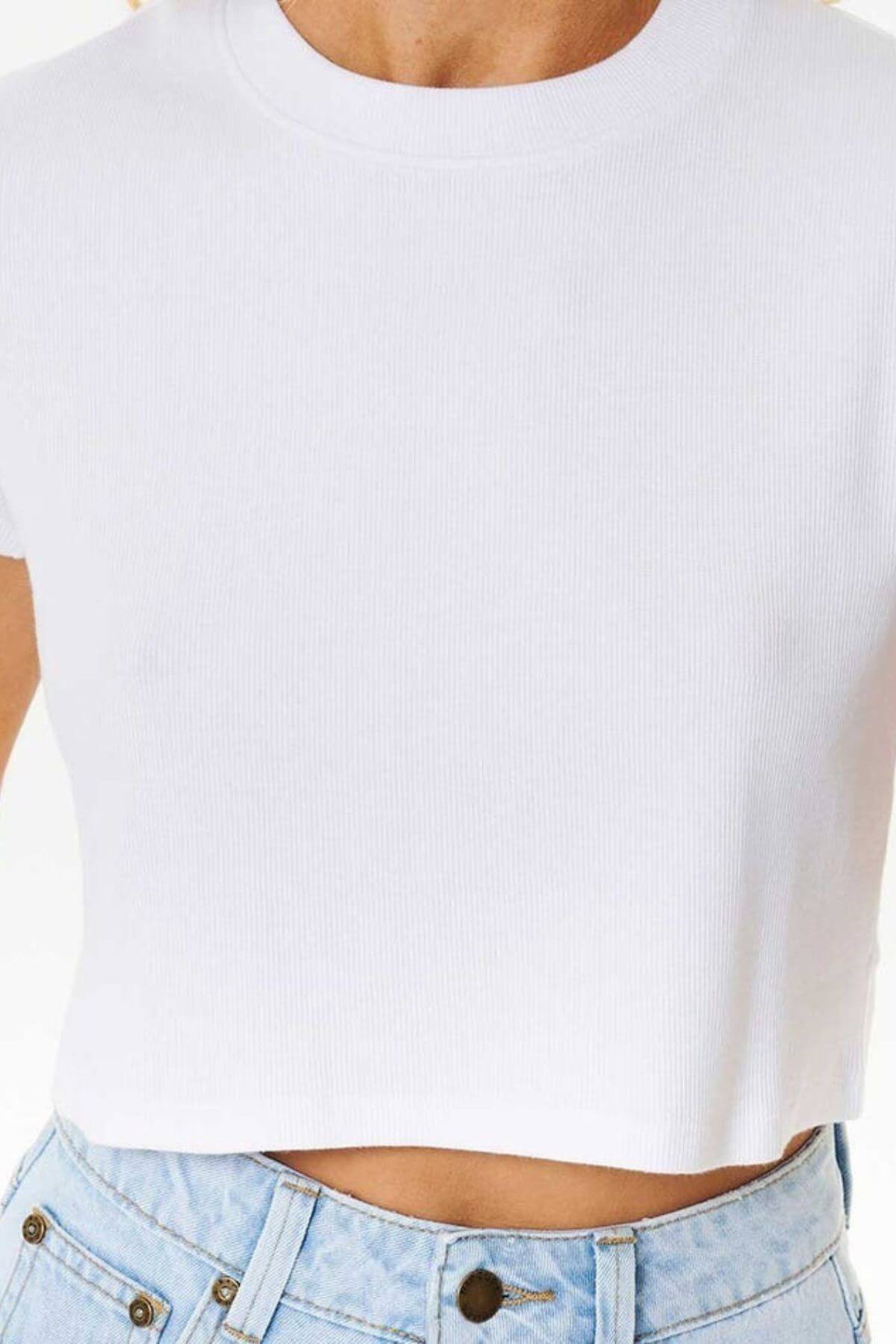 A person wears a Rip Curl Classic Ribbed Tee in white with high-waisted light blue jeans—truly a wardrobe essential.