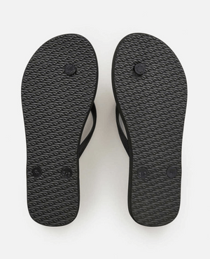A pair of Rip Curl La Isla Bloom Thongs, in black with textured soles, is displayed with the soles facing up. The right flip-flop shows noticeable wear on the heel area, while the left one appears less worn. Made with BLOOM™ algae blended foam for a sustainable touch, they are set against a plain white background.