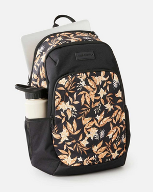 The Rip Curl Ozone 2.0 30L Backpack in recycled polyester features a beige and brown leaf print, holds a silver laptop in the main compartment and a white water bottle in the side pocket, shown against a plain light background.