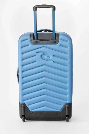 A blue Rip Curl F-Light Artist Of The Search Ty Williams 100L Global Travel Bag with diagonal ridges, a telescoping handle, and two wheels, shown against a plain white background.