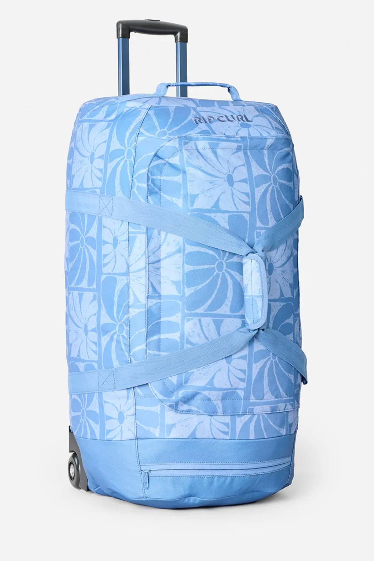 The Rip Curl Jupiter 80L Mixed Travel Bag is a large blue travel bag with floral patterns, telescoping handle, gray side straps, made from recycled polyester and stands upright on two wheels.