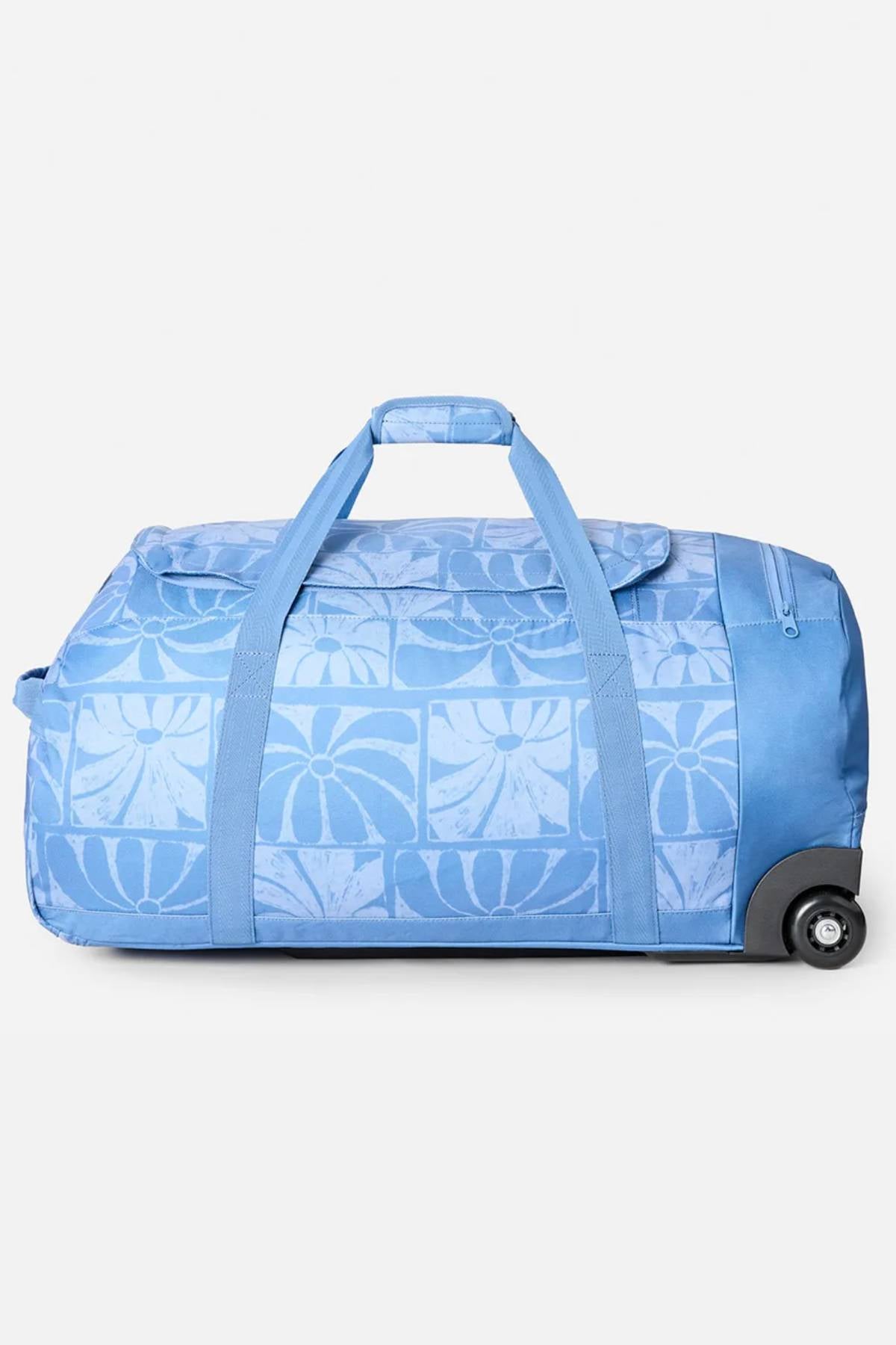 The Rip Curl Jupiter 80L Mixed Travel Bag is a spacious light blue travel bag with a floral design, made from recycled polyester. It has two handles, a zippered top, and wheels on one end for easy transport.