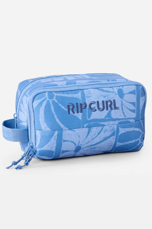 The Rip Curl Mixed Toiletry Bag is a rectangular blue travel bag with a floral pattern, embroidered front logo, side handle, two zip compartments, and matching blue zipper pulls.