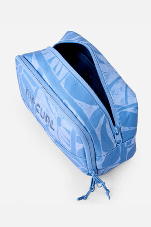The Rip Curl Mixed Toiletry Bag is light blue with abstract wave patterns and a bold butterfly design, featuring a zipper closure. The bag is partially open, showing its dark interior.