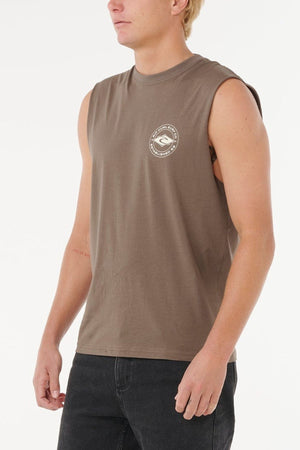 Wearing the Rip Curl Staple Muscle 100% cotton shirt with a small white circular logo on the left chest, paired with black jeans, a person stands against a plain white background.