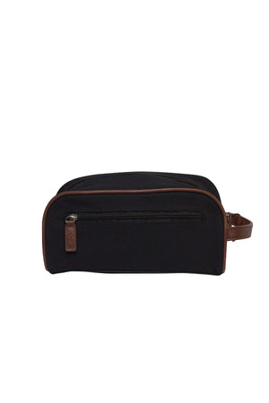 The Pilbara Toiletry Bag is a premium canvas black toiletry bag with brown accents and a leather handle on the right side. It features a small zippered pocket on the front and a main compartment with a zipper closure along the top, perfect for luxury travel.