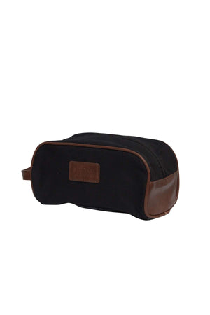 The Pilbara Toiletry Bag is a premium canvas toiletry bag featuring brown leather accents on the sides and edges, with a leather patch on one side. It includes a handle on one end and has a zipper running along the top, making it ideal for luxury travel.