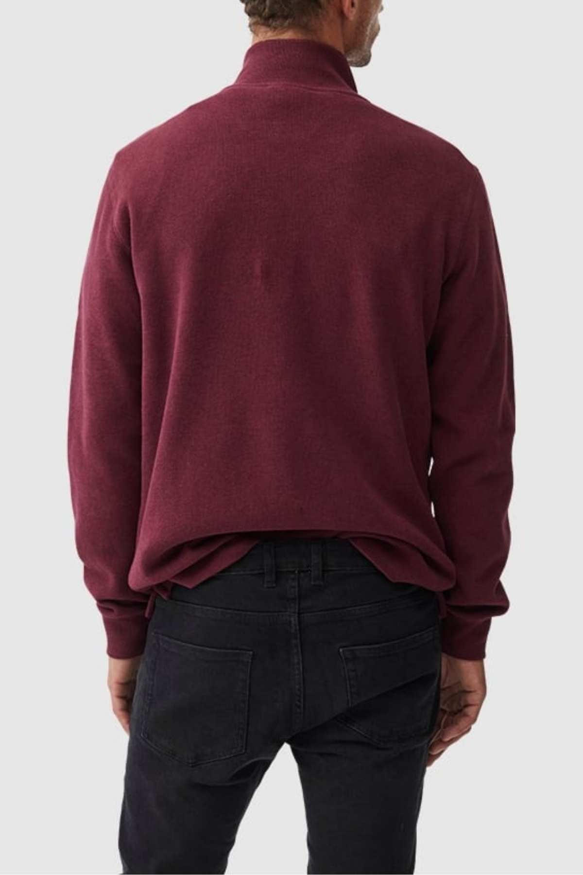 A man wearing a maroon Rodd & Gunn Alton Ave Sweat and black jeans stands facing away, displaying the back of his outfit against a plain light gray background.