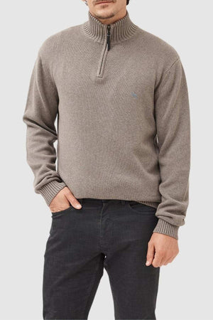 A man in the Rodd & Gunn Merrick Bay Knit, made from 100% cotton with a premium YKK zip, and dark jeans stands with one hand in his pocket against a plain light background.