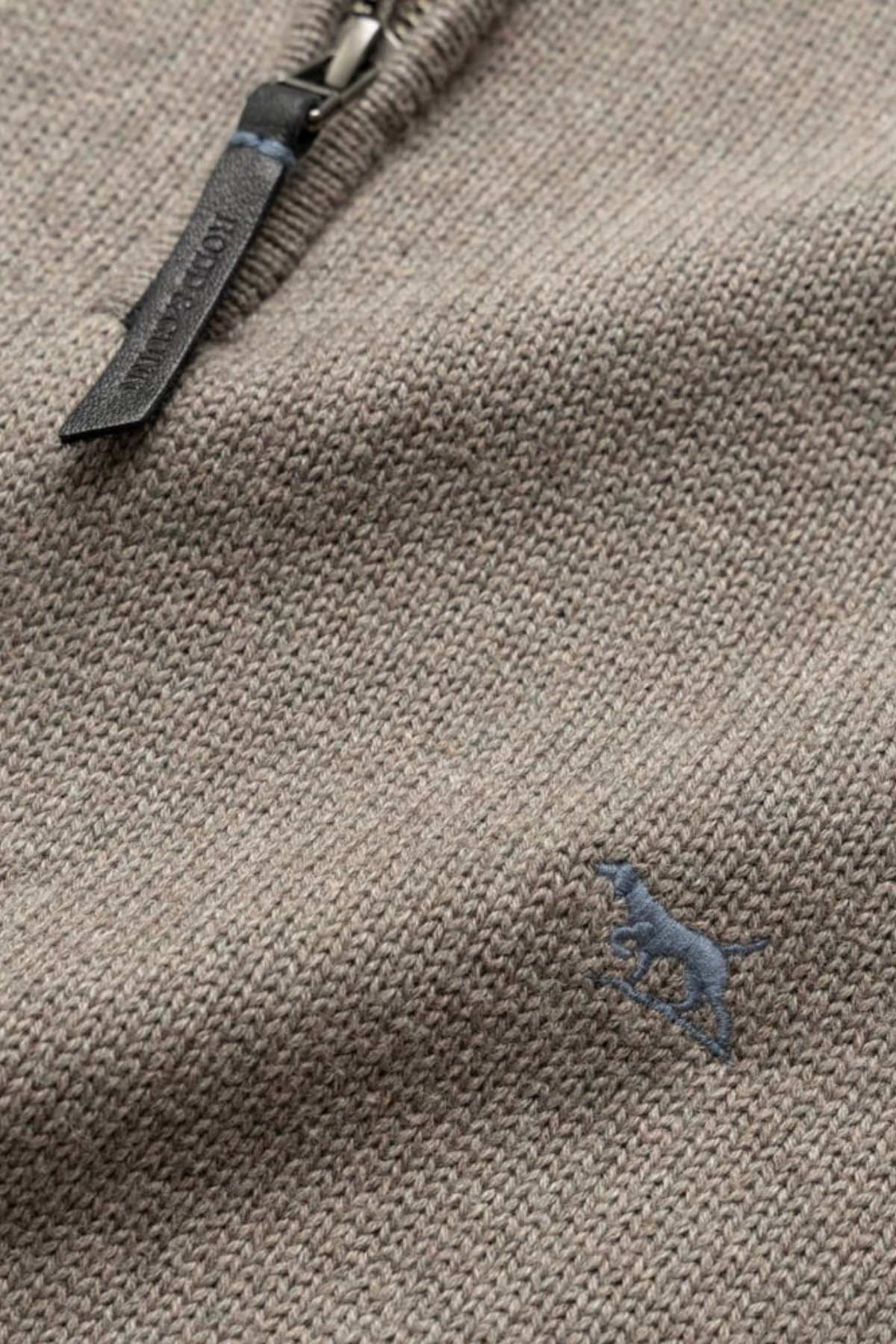 Close-up of the Rodd & Gunn Merrick Bay Knit sweater in beige 100% cotton, showing its textured knit, small blue embroidered dog logo, and premium YKK zip with leather pull tab.