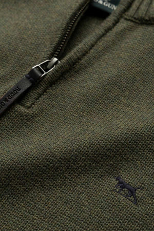 Detailed view of the Rodd & Gunn Merrick Bay Knit shows its textured olive green 100% cotton fabric, a premium black YKK half-zipper with visible stitching, and a small embroidered dog logo in dark color on the lower right.