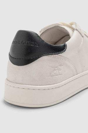 Close-up of the heel of the Rodd & Gunn Sussex Street Sneaker, a white shoe with a black leather accent and embossed logo. "RODD & GUNN" text is on the back. The durable rubber outsole rests on a light gray background.