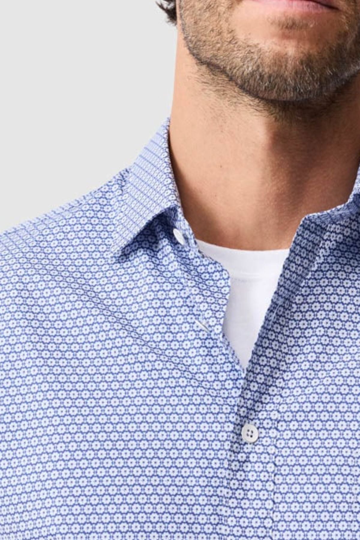 Close-up of a man wearing the Rodd & Gunn Blumine Sports Fit Shirt, a blue and white slim fit 100% cotton shirt over a white tee. Only his lower face, neck, and upper torso are shown against a light gray background.
