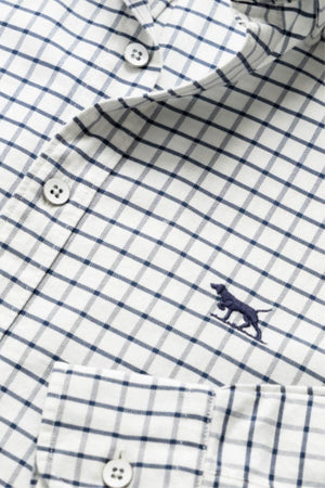 A close-up of the Rodd & Gunn Gunn Check Oxford 3 Sports Fit Shirt in white with a blue check pattern, featuring white buttons, a front pocket, and a small blue embroidered dog logo on the chest.