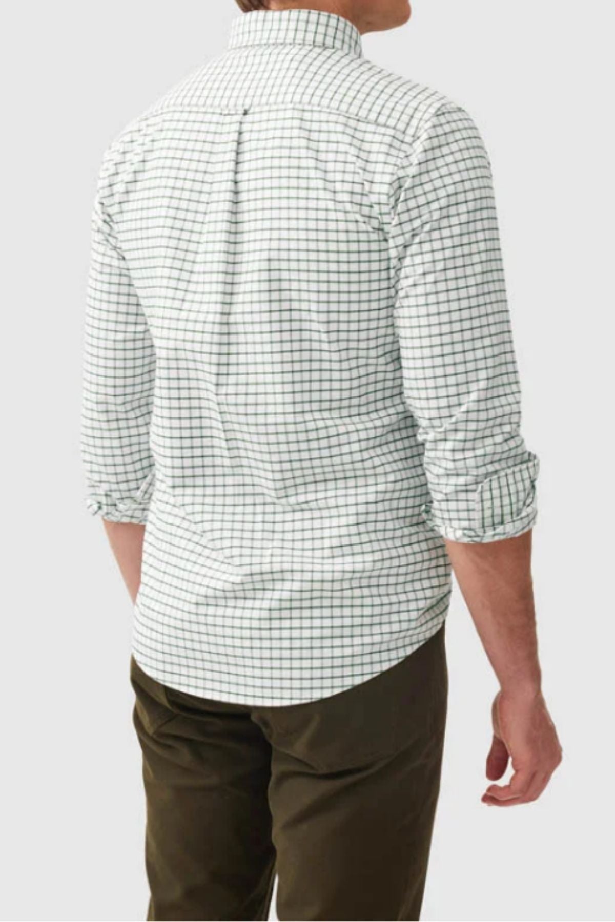 A man is seen from behind wearing the Rodd & Gunn Gunn Check Oxford 3 Sports Fit Shirt in green check, paired with olive green pants. His sleeves are rolled up as he stands against a plain light gray background.