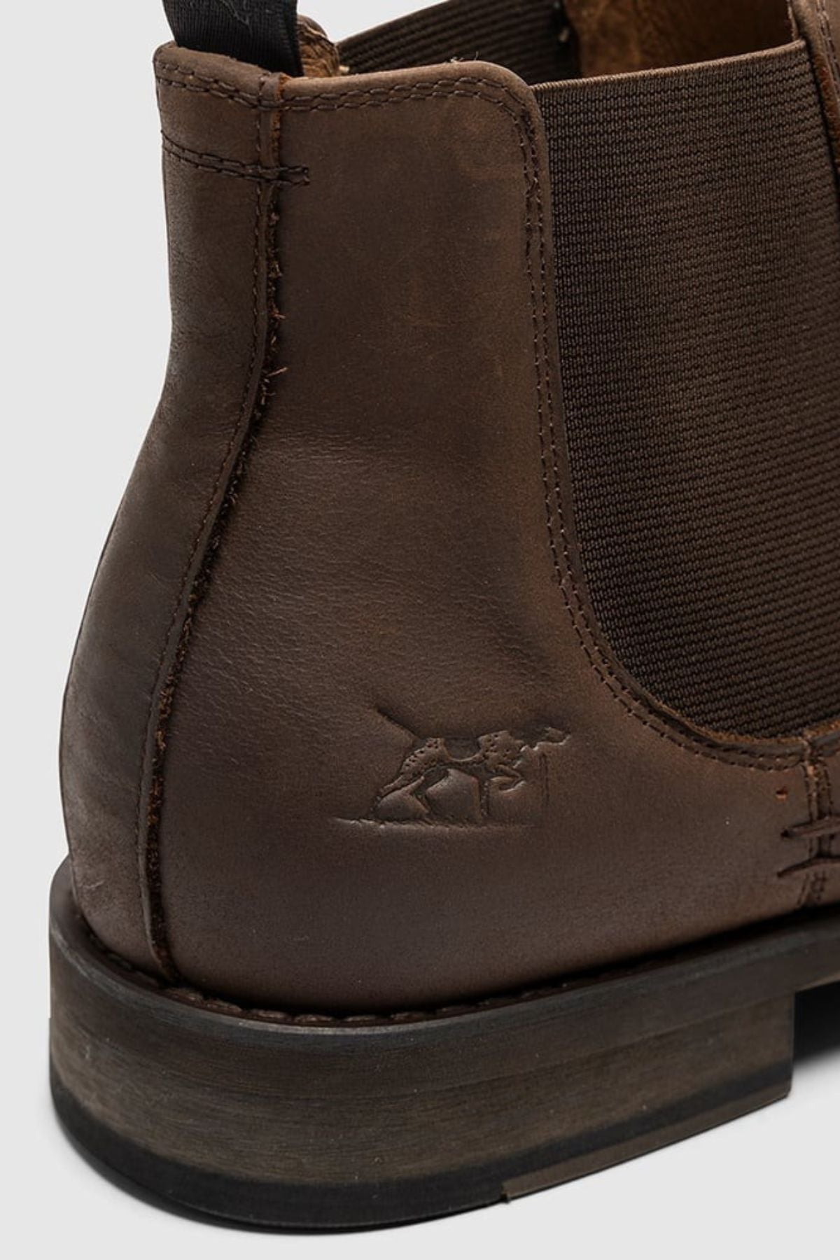 Close-up of the Rodd & Gunn Ealing Chelsea Boot’s heel and side in brown oiled leather, featuring an elastic panel, detailed stitching, a small embossed camel logo by the heel, and a flexible rubber outsole for comfort.