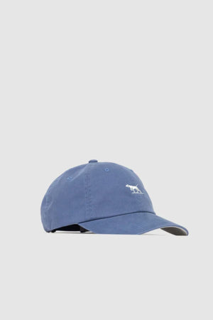 The Rodd & Gunn Gunn Cap is a blue cotton twill cap with a curved brim and a small white embroidered pointer dog logo on the front, shown against a plain light gray background.
