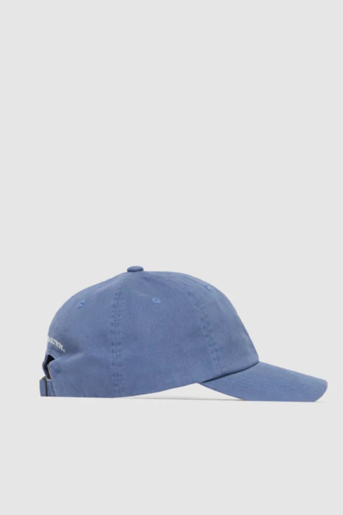 The Rodd & Gunn Gunn Cap is a blue cotton twill cap with a curved brim, adjustable back strap, and ventilation eyelets. It features the signature pointer dog logo and is shown from the side on a plain light background.