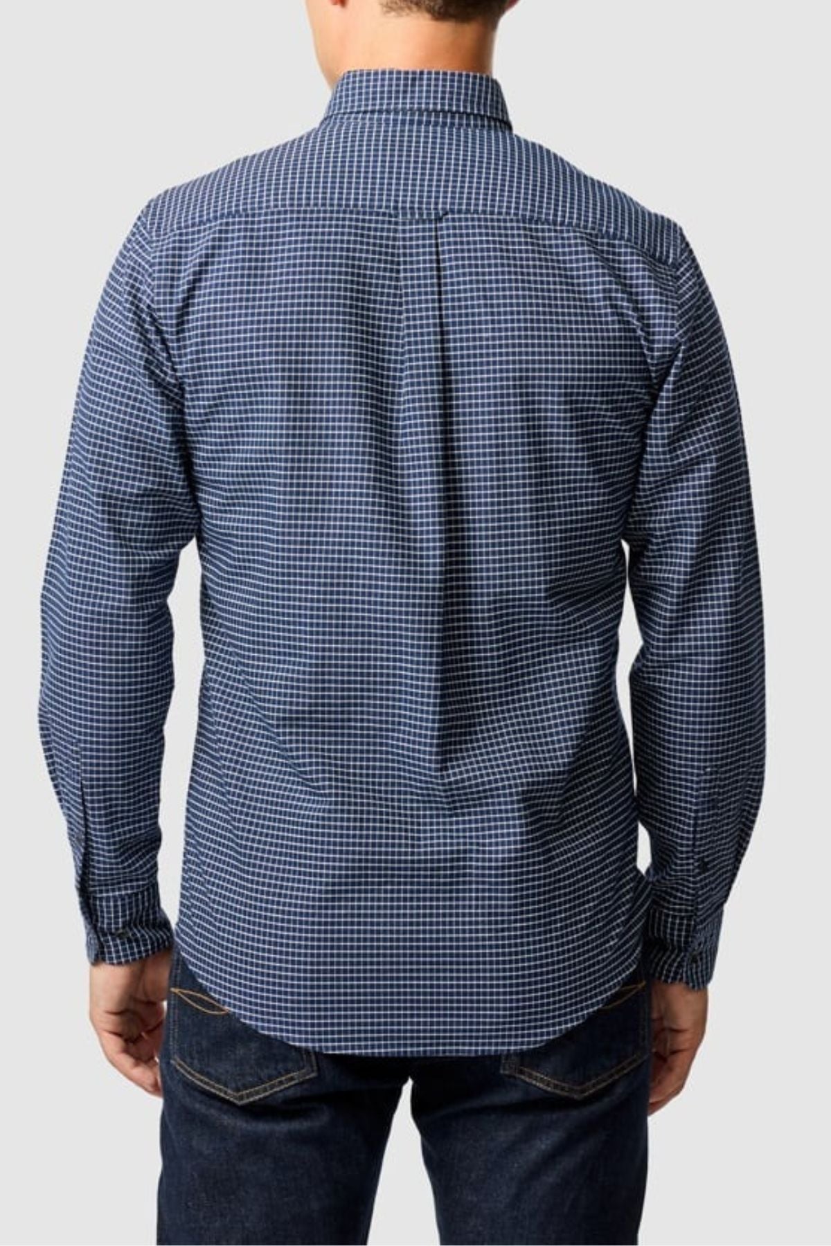A person is seen from the back, wearing a blue and white Rodd & Gunn Gunn Check Oxford 5 Sports Fit Shirt with dark jeans, set against a plain light gray background.