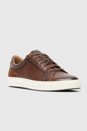 The Rodd & Gunn Transit Sneaker features brown leather, matching laces, and a white rubber sole, shown on a plain light gray background.