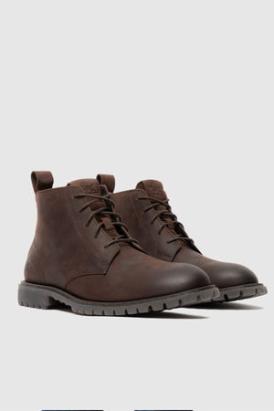 The Rodd & Gunn Clearview Chukka Boot, crafted from dark brown USA crazyhorse leather with translucent rubber outsoles, is shown on a light grey background, angled to highlight both the front and side views.