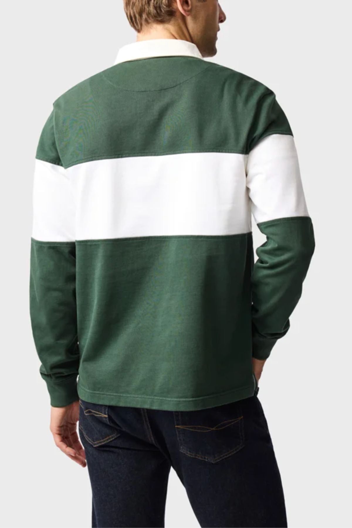 A person is seen from the back wearing the Rodd & Gunn Foresters Rugby—a green mid-weight jersey with a bold white stripe across the chest and upper arms—paired with dark blue jeans, set against a plain light gray background.