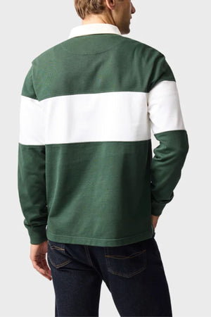 A person is seen from the back wearing the Rodd & Gunn Foresters Rugby—a green mid-weight jersey with a bold white stripe across the chest and upper arms—paired with dark blue jeans, set against a plain light gray background.