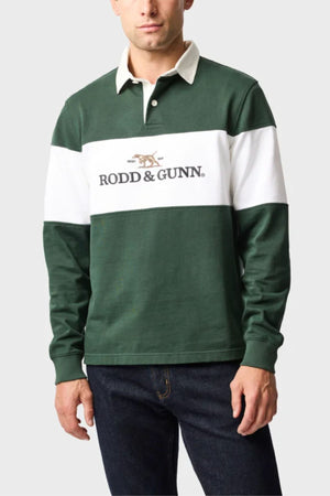 A man wears the Rodd & Gunn Foresters Rugby, a green and white 100% cotton long-sleeve jersey with a beige collar and "RODD & GUNN" logo on the chest, paired with dark jeans against a plain background.