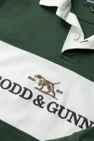 Close-up of the Rodd & Gunn Foresters Rugby shirt in green and white 100% cotton jersey, showing part of the collar, buttons, “RODD & GUNN” text, an embroidered dog logo, and “REGO. 1848” on the white stripe.