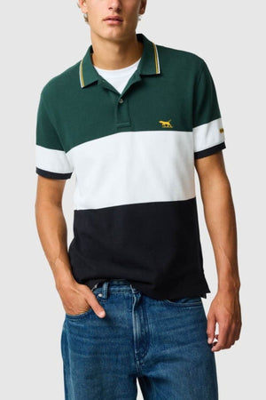 A person wears a green, white, and black color-blocked Rodd & Gunn Homebay Polo made from Australian Good Earth Cotton, featuring yellow trim and a small yellow animal logo, paired with blue jeans against a plain light background.