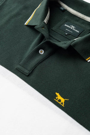 A close-up of the Rodd & Gunn Homebay Polo, a green and white sports-fit shirt with a yellow dog logo on the chest and yellow collar trim, showcasing sustainable men's fashion and Rodd & Gunnās label inside the collar.