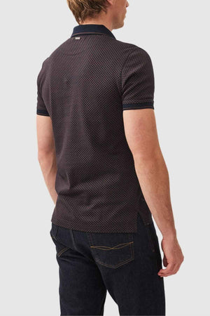 Wearing the Rodd & Gunn Lynden Sports Fit Polo, a man stands facing away in dark jeans. The polo, made from premium cotton yarn with a textured pattern, contrasts against a light gray background.