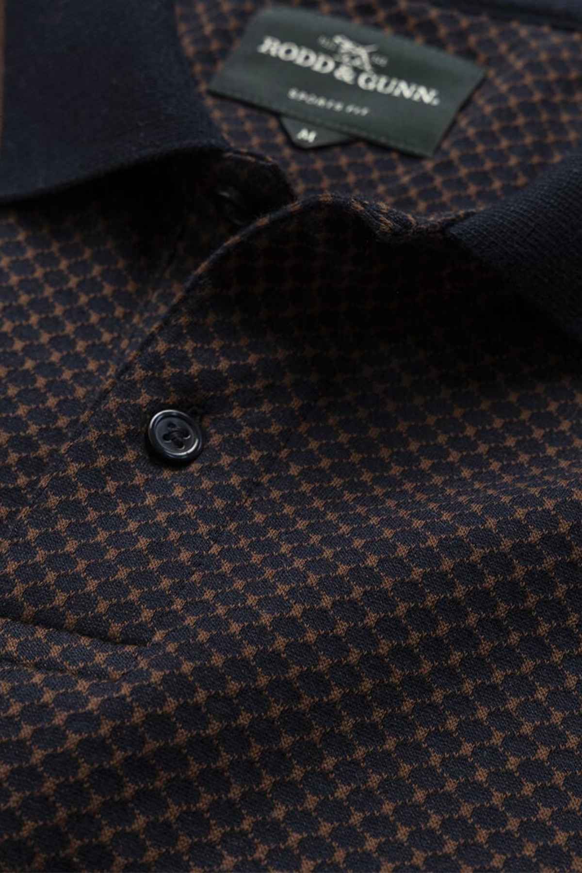 Close-up of a dark-colored houndstooth patterned shirt with black buttons. A label, partially visible at the neckline, is sewn inside the collar, indicating that it is a Rodd & Gunn Lynden Sports Fit Polo made from premium cotton yarn and displays the shirt size.