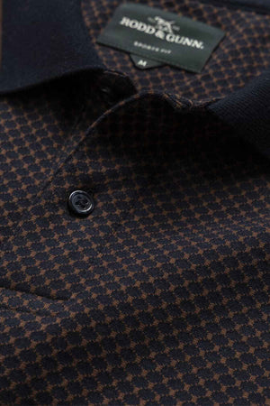Close-up of a dark-colored houndstooth patterned shirt with black buttons. A label, partially visible at the neckline, is sewn inside the collar, indicating that it is a Rodd & Gunn Lynden Sports Fit Polo made from premium cotton yarn and displays the shirt size.