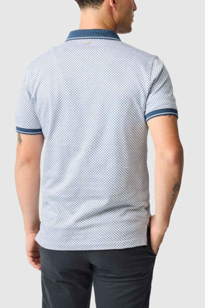 A person wearing a Rodd & Gunn Lynden Sports Fit Polo in light blue polka dot, crafted from luxurious Turkish cotton, with dark blue trim, and paired with dark pants is standing facing away against a plain gray background.