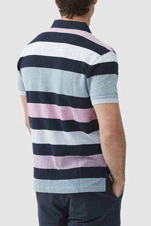 Someone stands with their back to the camera, wearing a Rodd & Gunn Solomons Point Sports Fit Polo with wide dark blue, pink, light gray, and white stripes. Made from 100% cotton with four-way stretch for comfort, they have one hand in their pocket against a plain light gray background.