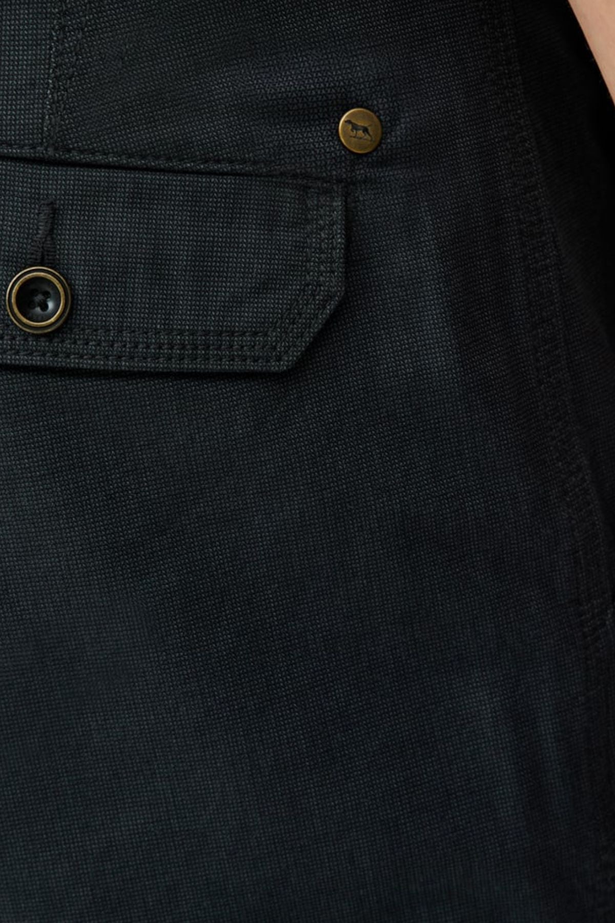 Close-up of Rodd & Gunn The Gunn Short in a dark cotton-elastane blend, showcasing its textured fabric, buttoned flap pocket, and small brass rivet—signature details of classic fit shorts.
