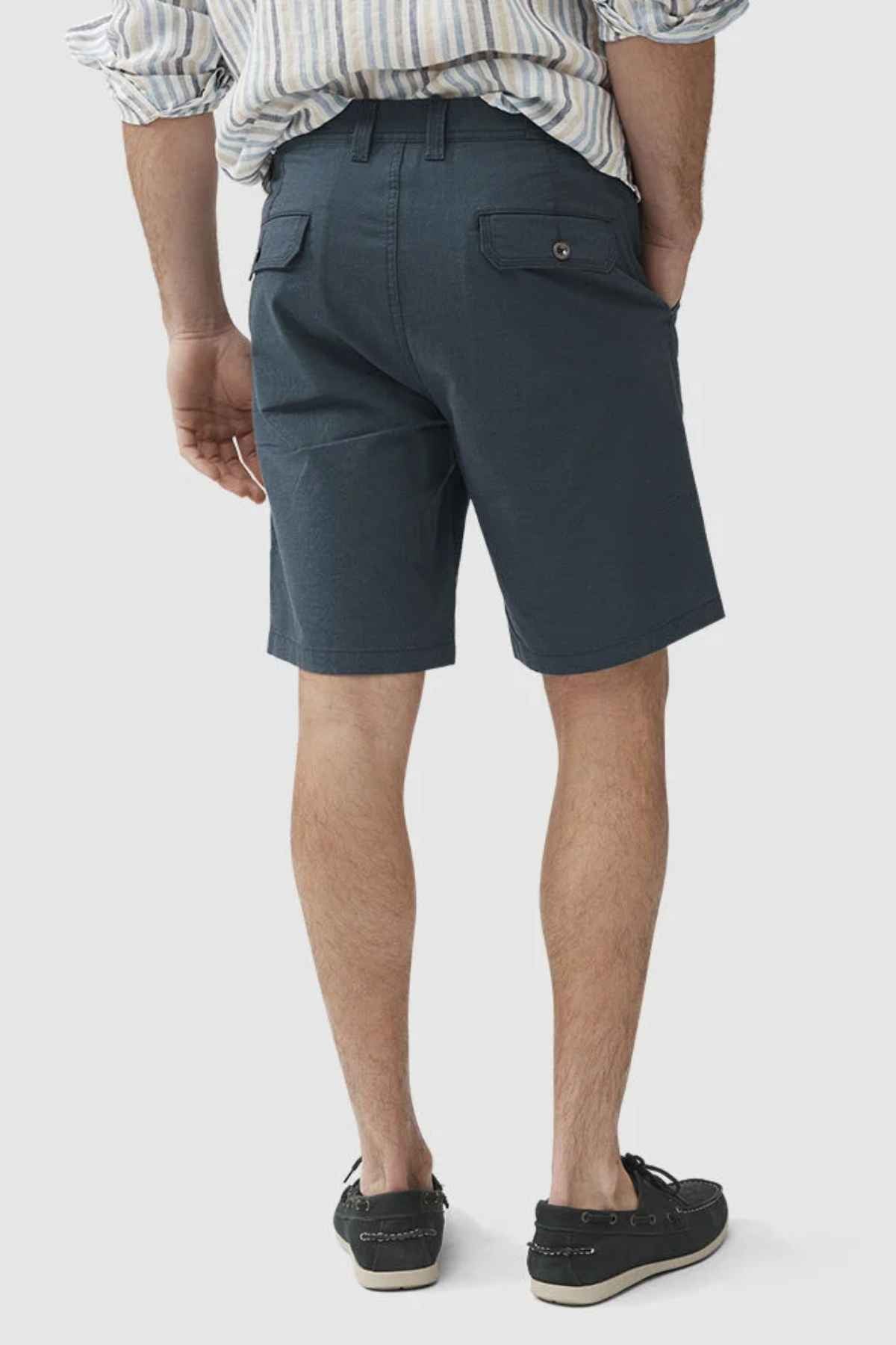 A person is wearing a striped shirt crafted from high-quality cotton, paired with dark green Rodd & Gunn The Gunn Shorts that boast an original fit, and black loafers. They are standing with their back facing the camera against a plain white background.