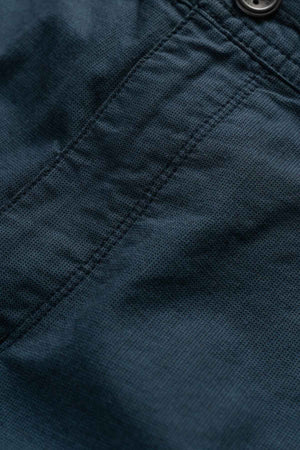 Close-up of the Rodd & Gunn The Gunn Short's dark fabric, showcasing a visible stitched seam with a button at the top right. The high-quality cotton texture appears coarse, hinting at its durable material. The seam runs vertically through the center, emphasizing its original fit design.