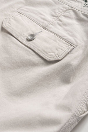 Close-up of a beige fabric pocket with a flap and single button on a piece of clothing. The material, part of Rodd & Gunn The Gunn Short, appears soft and exhibits neat stitching around the edges of the pocket and flap, epitomizing the quality craftsmanship in these classic fit shorts from Rodd & Gunn.