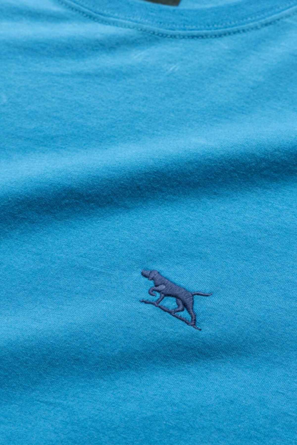 Close-up of the Rodd & Gunn The Gunn T-Shirt, a blue casual tee in soft Australian cotton, featuring a small, dark blue embroidered walking dog logo on the chest.