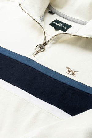 A close-up of the Rodd & Gunn Chesterfield Sweat in cream, featuring blue and navy stripes, a metallic ring zipper, an embroidered dog logo, and crafted with Good Earth Cotton. The Rodd & Gunn brand tag is visible inside the collar.